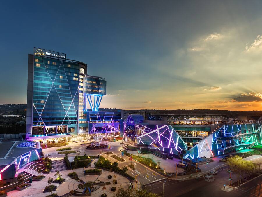 A hotel with a modern design, featuring a prominent Time Square sign, a spacious courtyard, and a unique architectural structure with illuminated geometric patterns.