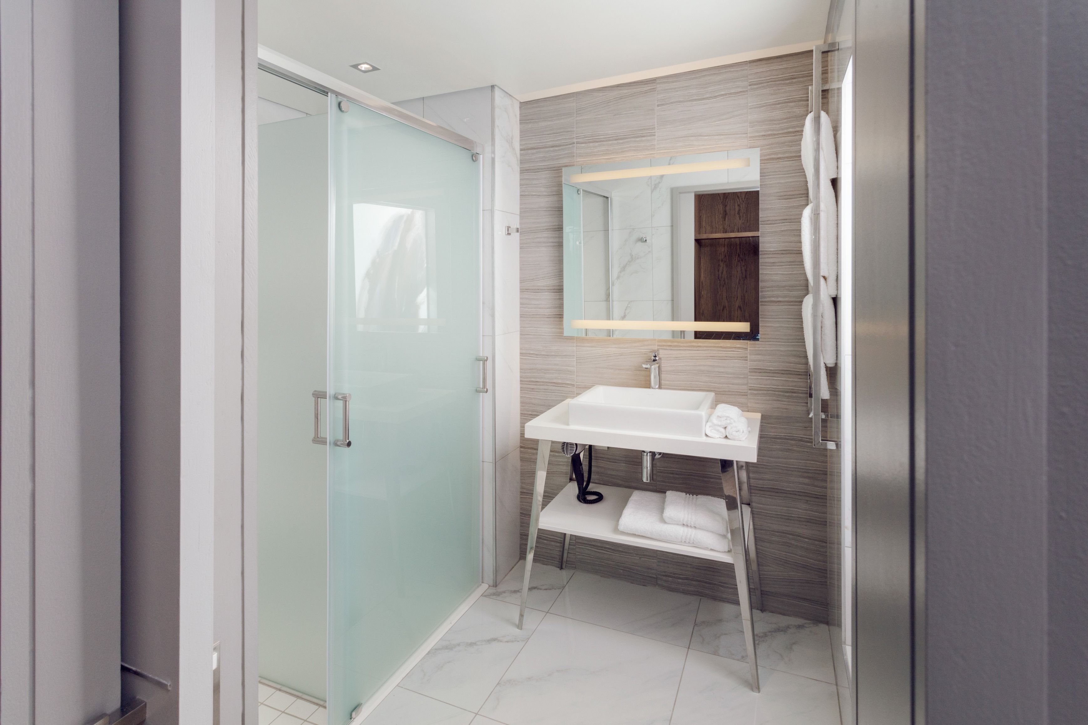 A modern bathroom with a glass shower enclosure, a white sink, and a wooden vanity.