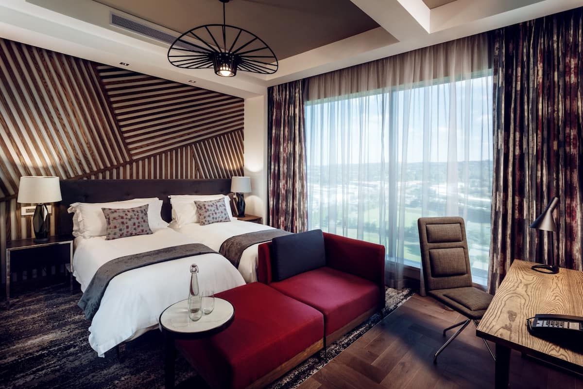 A hotel room with a large bed, a red sofa, a wooden desk, and a view of the city.