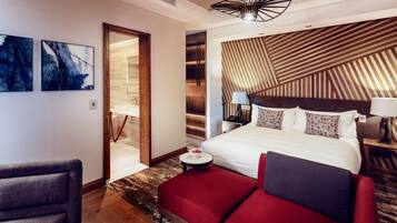 A modern hotel room with a large bed, a red sofa, a wooden slatted headboard, and abstract wall art.