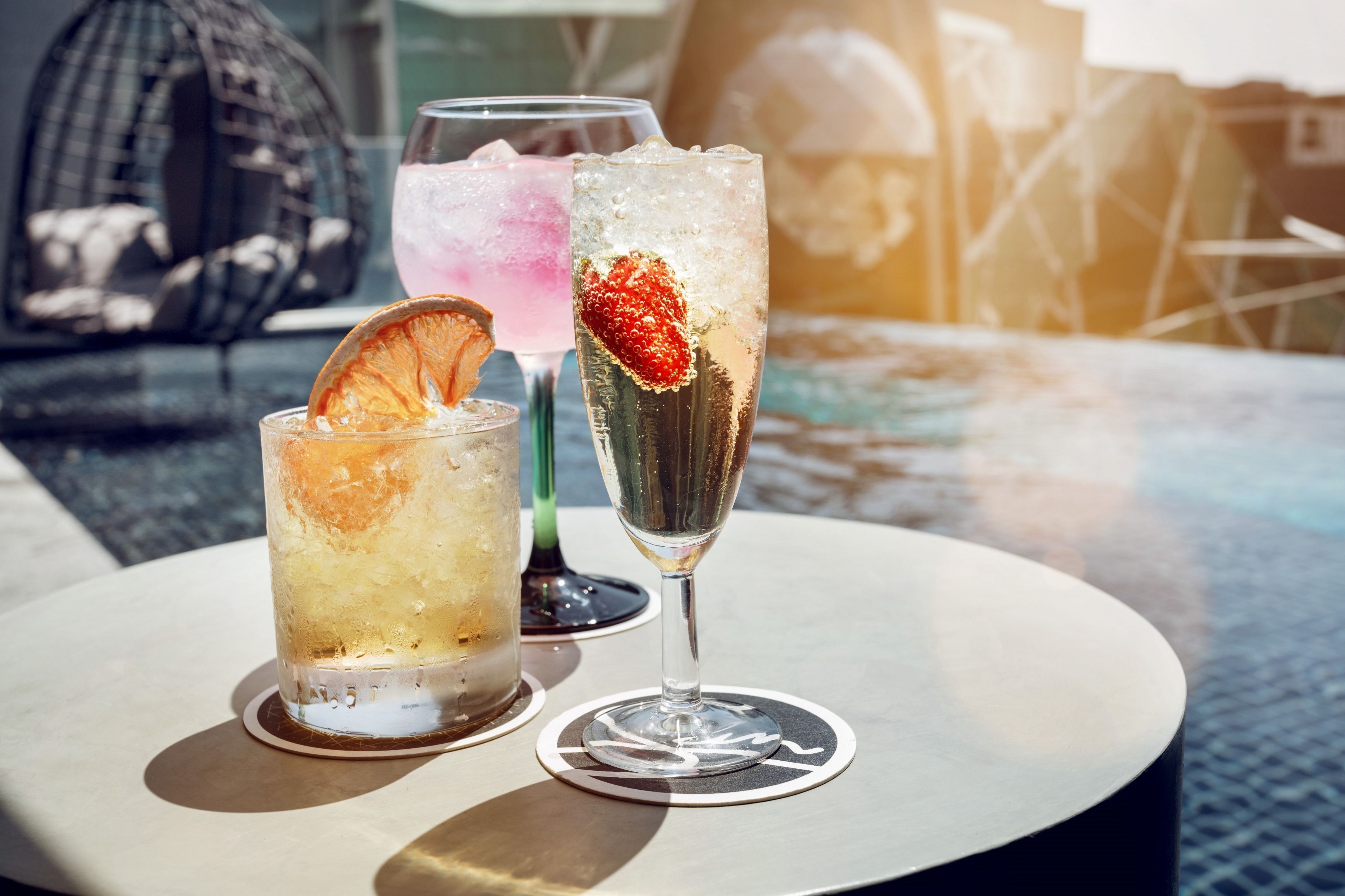Three glasses of beverages on a round table with a bird sculpture in the background.