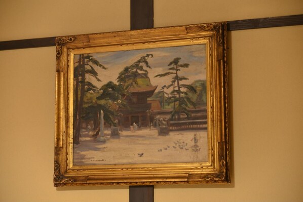 Un tableau encadré représentant un bâtiment traditionnel avec une pagode, entouré d’arbres et de personnes.