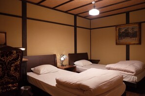 A hotel room with two single beds, a nightstand with a lamp, a chair, and a painting on the wall. - Guesthouse Bokuyado - Hostel (Kyoto)
