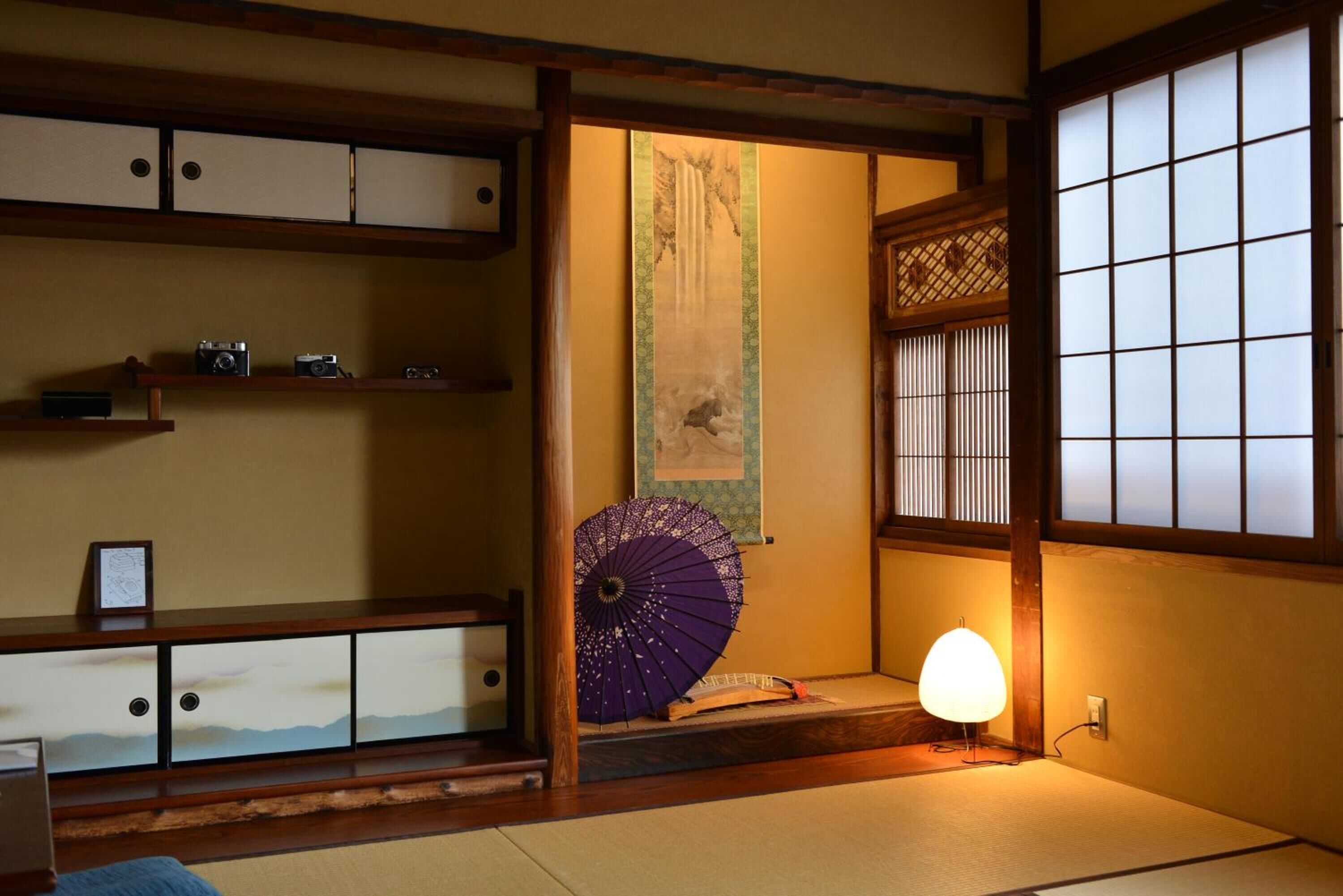 A traditional Japanese room with tatami flooring, a shoji screen, a hanging scroll, and a purple folding fan.