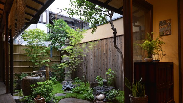 A traditional Japanese garden with a wooden fence, stone lanterns, and various plants. - Guesthouse Bokuyado - Hostel (Kyoto)
