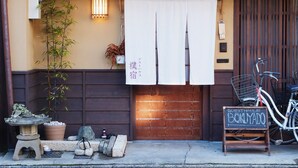 A traditional Japanese guesthouse with a wooden door, a signboard, and a bicycle parked outside. - Guesthouse Bokuyado - Hostel (Kyoto)