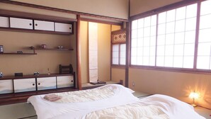A traditional Japanese-style room with tatami flooring, a low wooden bed with white bedding, and a sliding door leading to a traditional Japanese room. - Guesthouse Bokuyado - Hostel (Kyoto)