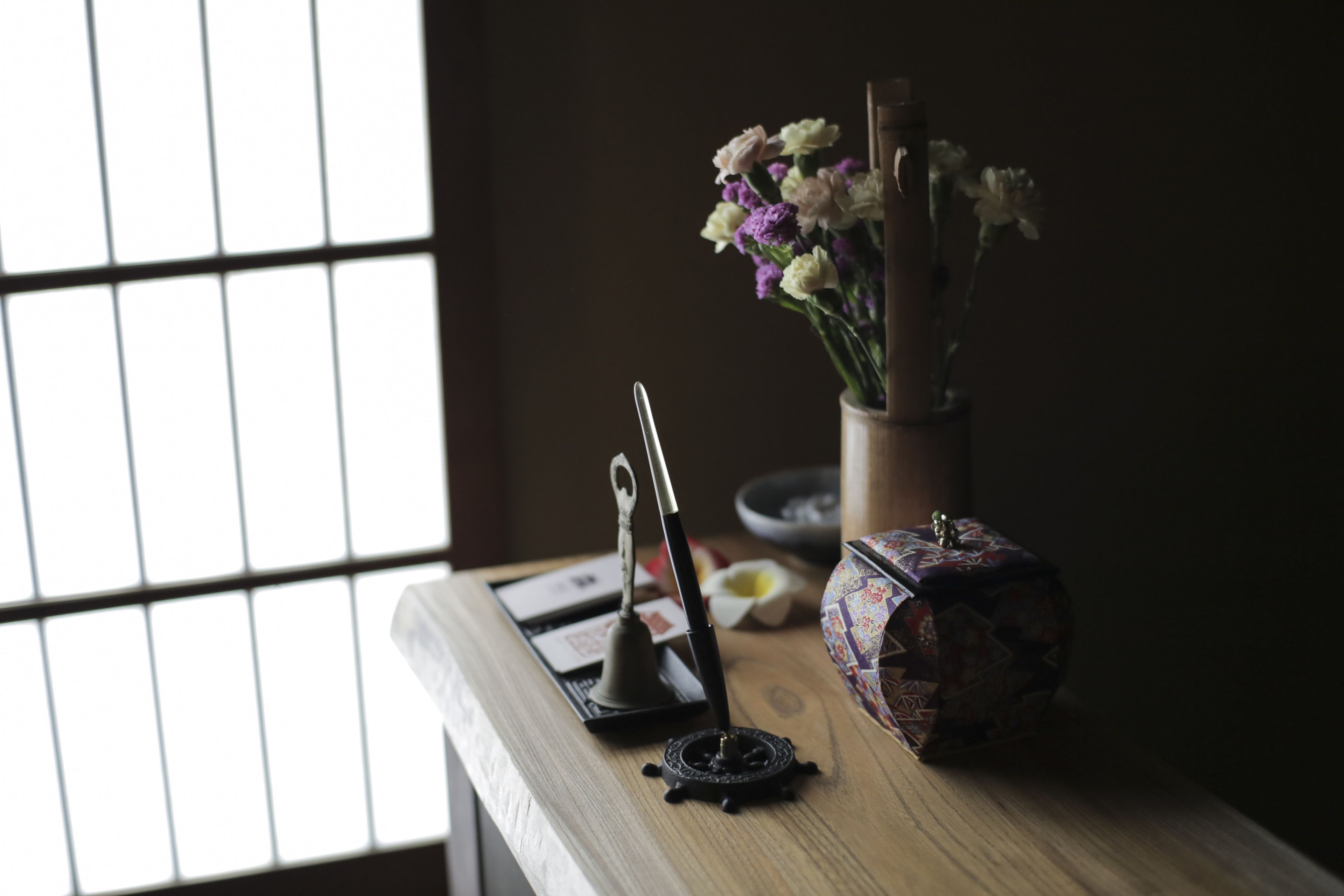 A wooden table with a vase of flowers, a decorative box, and a bell.