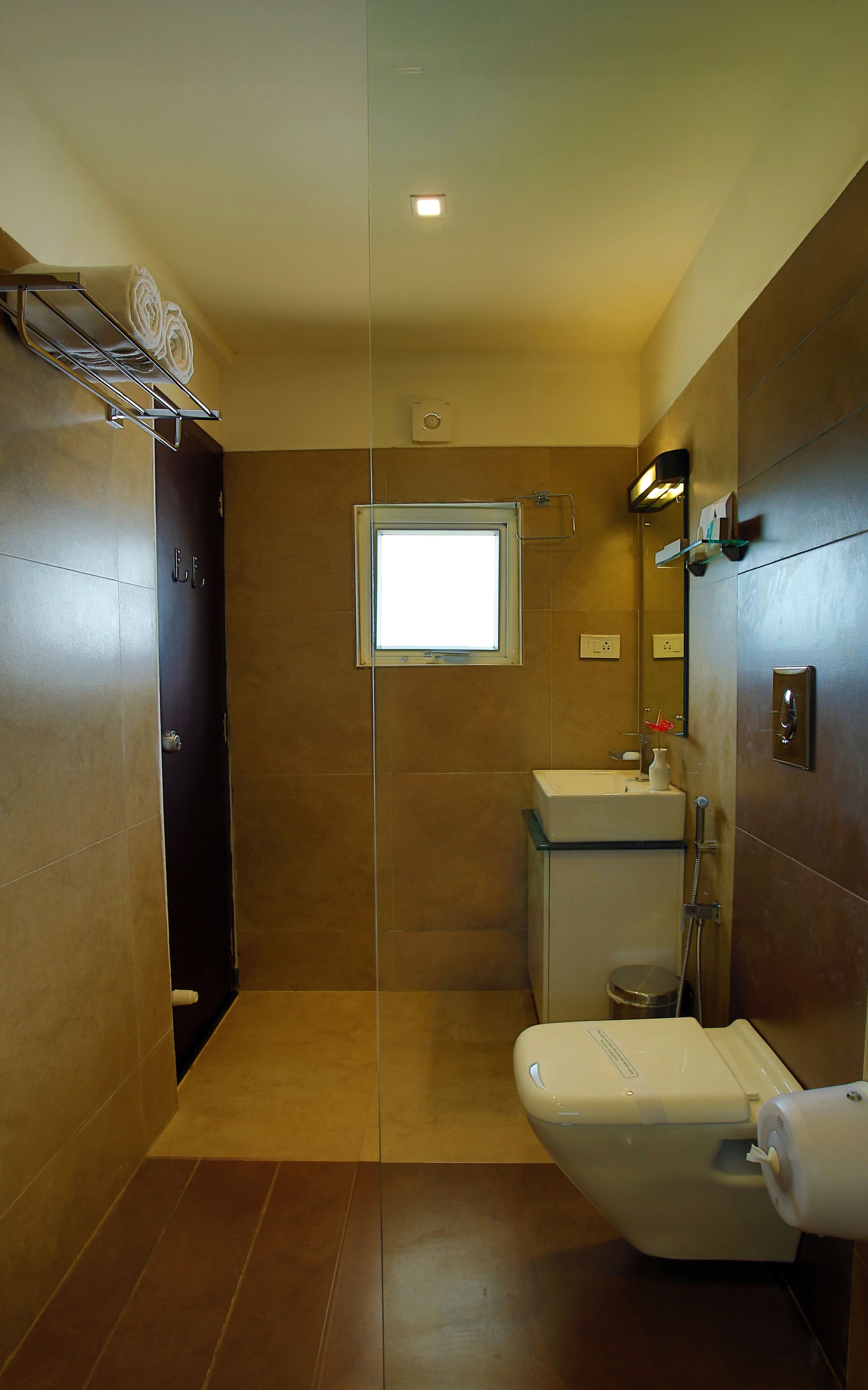 A modern bathroom with a toilet, sink, and shower. There is a window providing natural light and a towel rack with folded towels.
