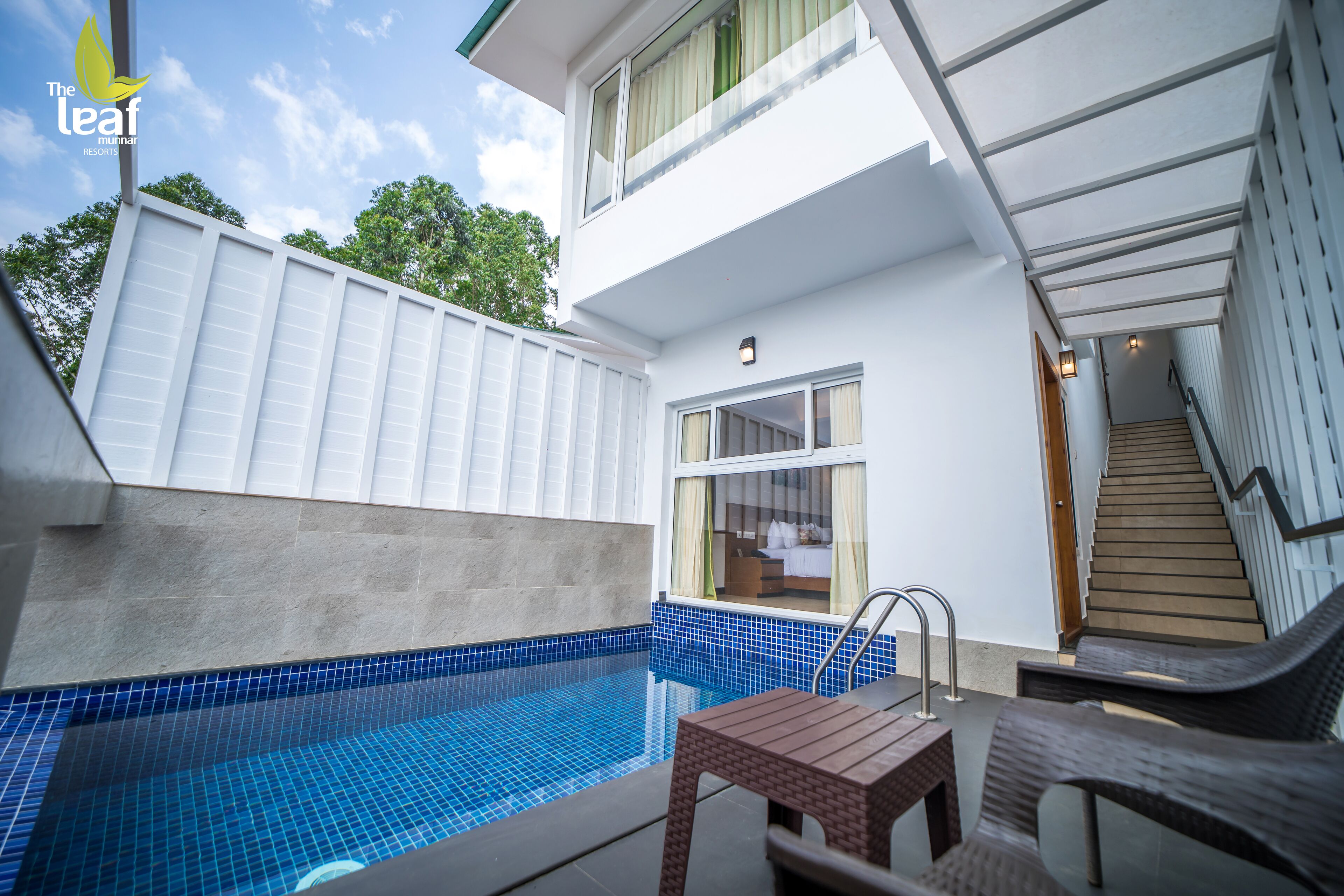 A modern hotel with a swimming pool, a covered outdoor seating area, and a staircase leading to the upper floor.