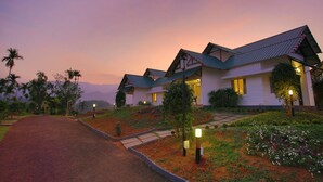 A row of modern houses with sloped roofs, surrounded by well-maintained gardens and palm trees, under a twilight sky. - The Leaf Munnar Resort (Devikolam)