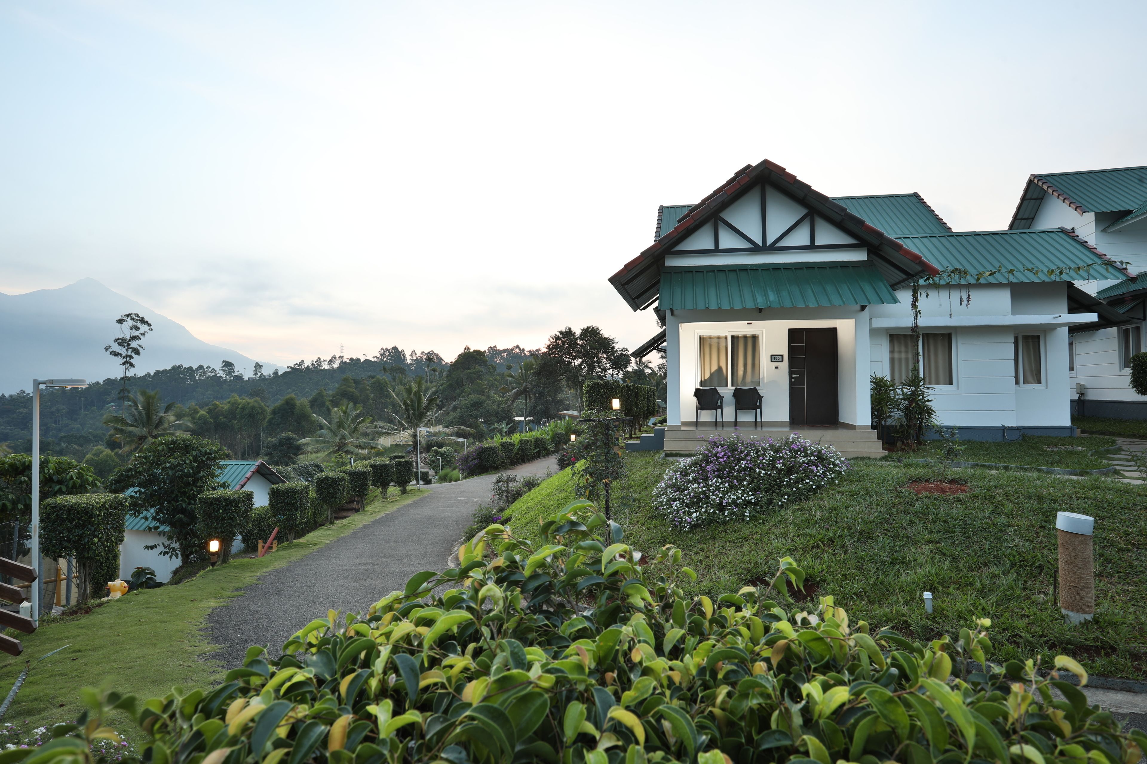 A modern hotel with a green roof, a paved driveway, and lush landscaping.