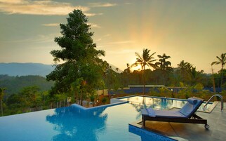 An infinity pool with a lounge chair, surrounded by lush greenery and palm trees, with a sunset in the background.