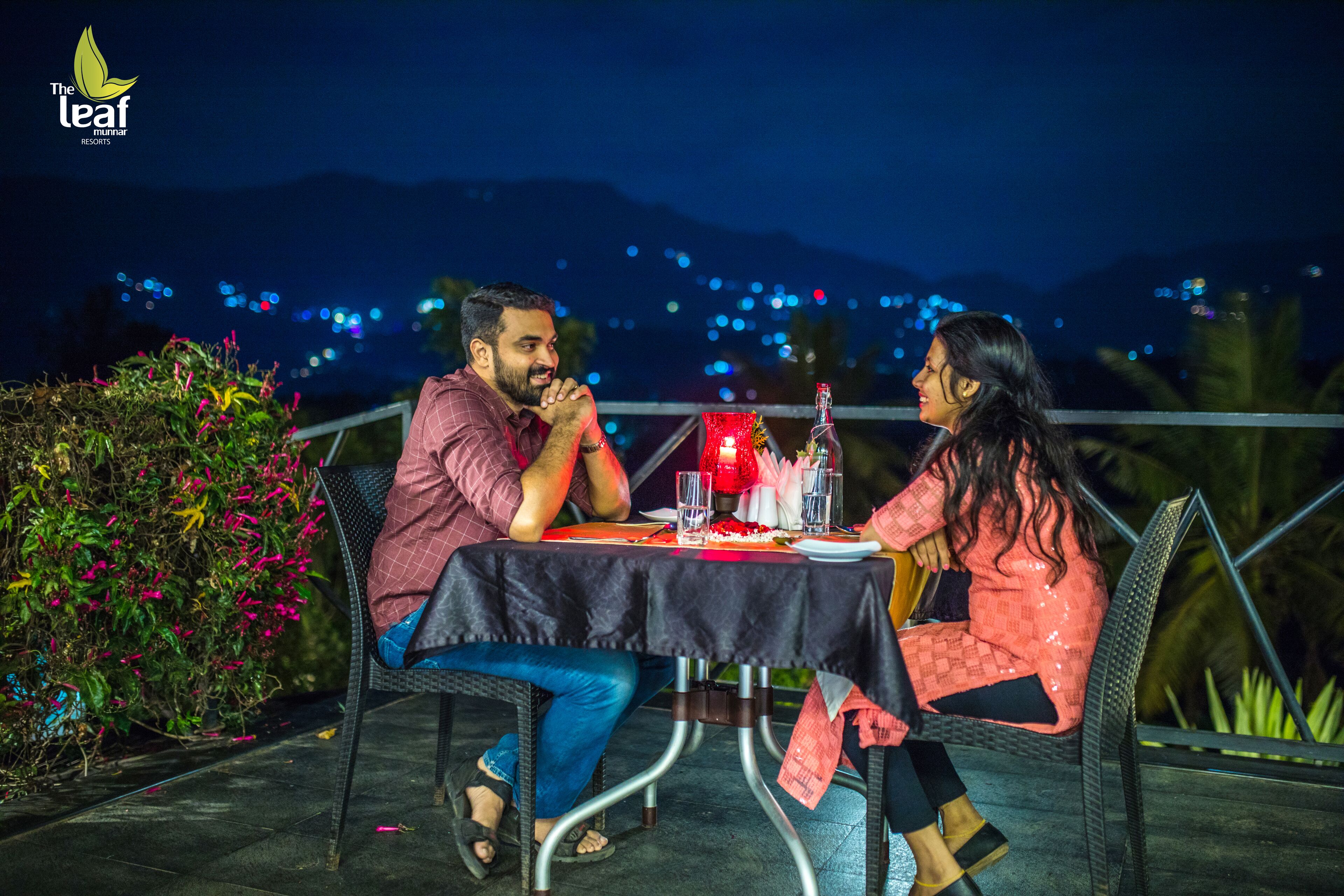 Un couple est assis à une table en plein air, avec une vue sur les montagnes en arrière-plan.