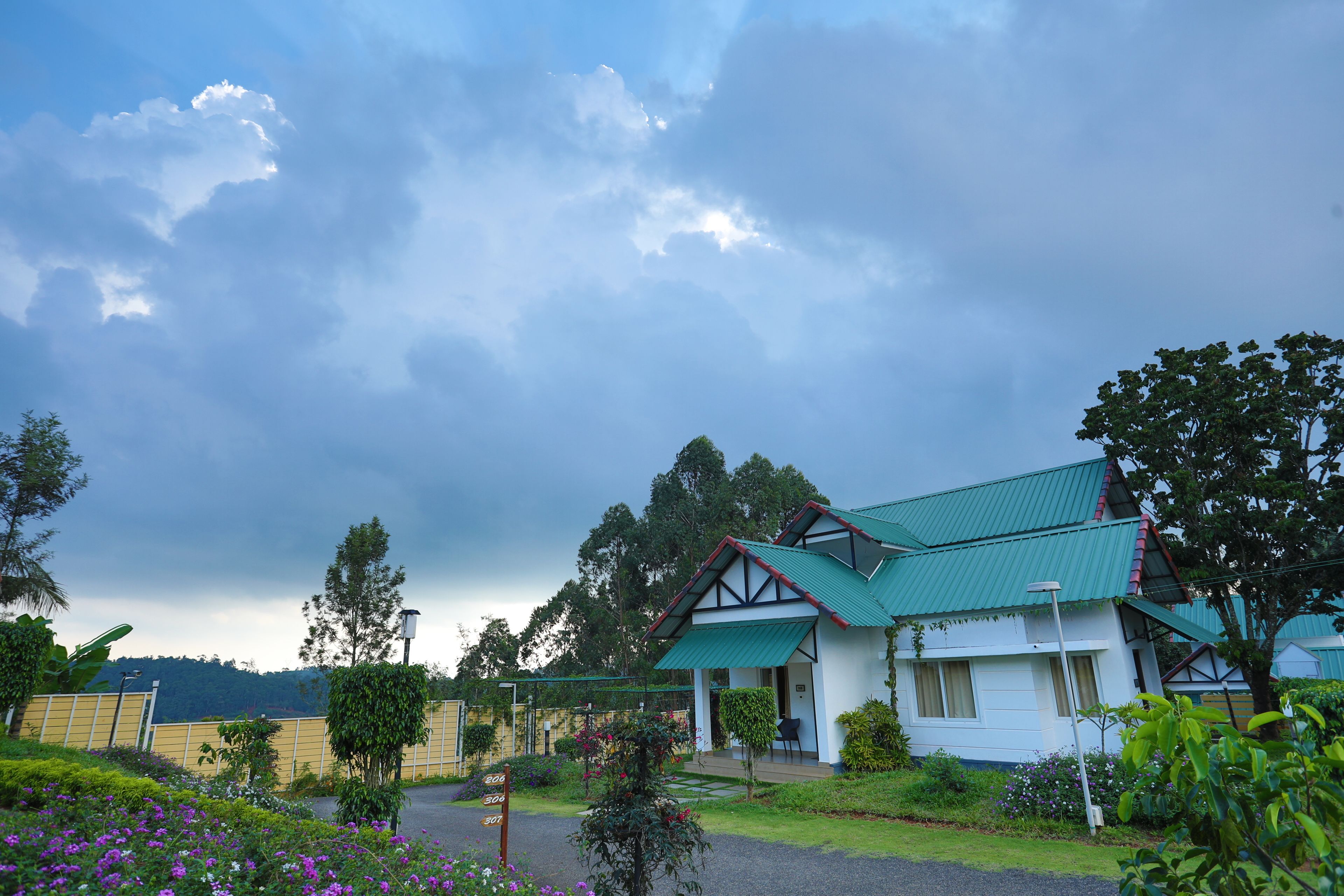 A traditional house with a green roof, surrounded by lush gardens and a cloudy sky.