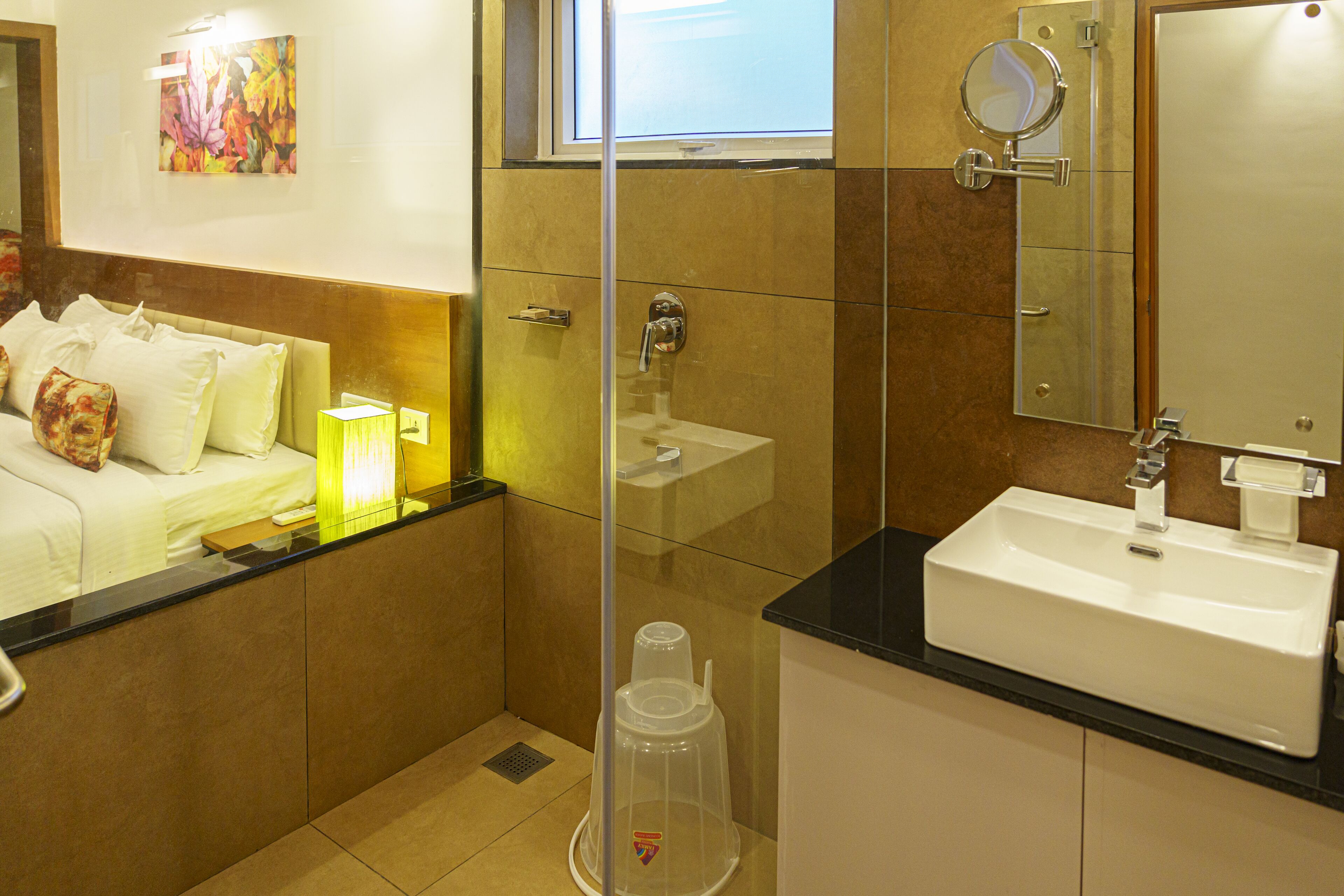 A modern bathroom with a glass shower enclosure, a white sink, and a bed with white bedding.