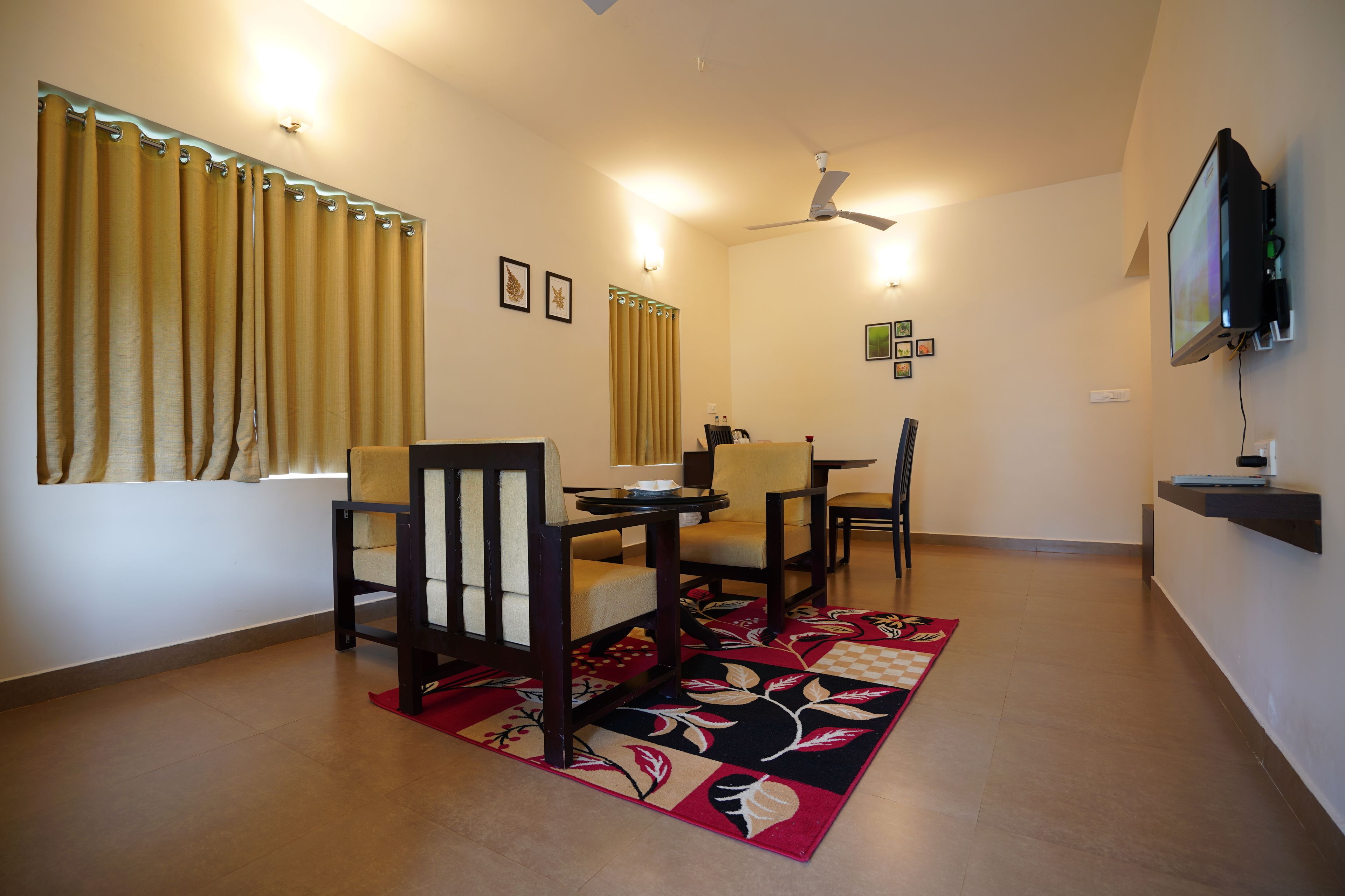 A dining area with a table, chairs, a patterned rug, and a television mounted on the wall.