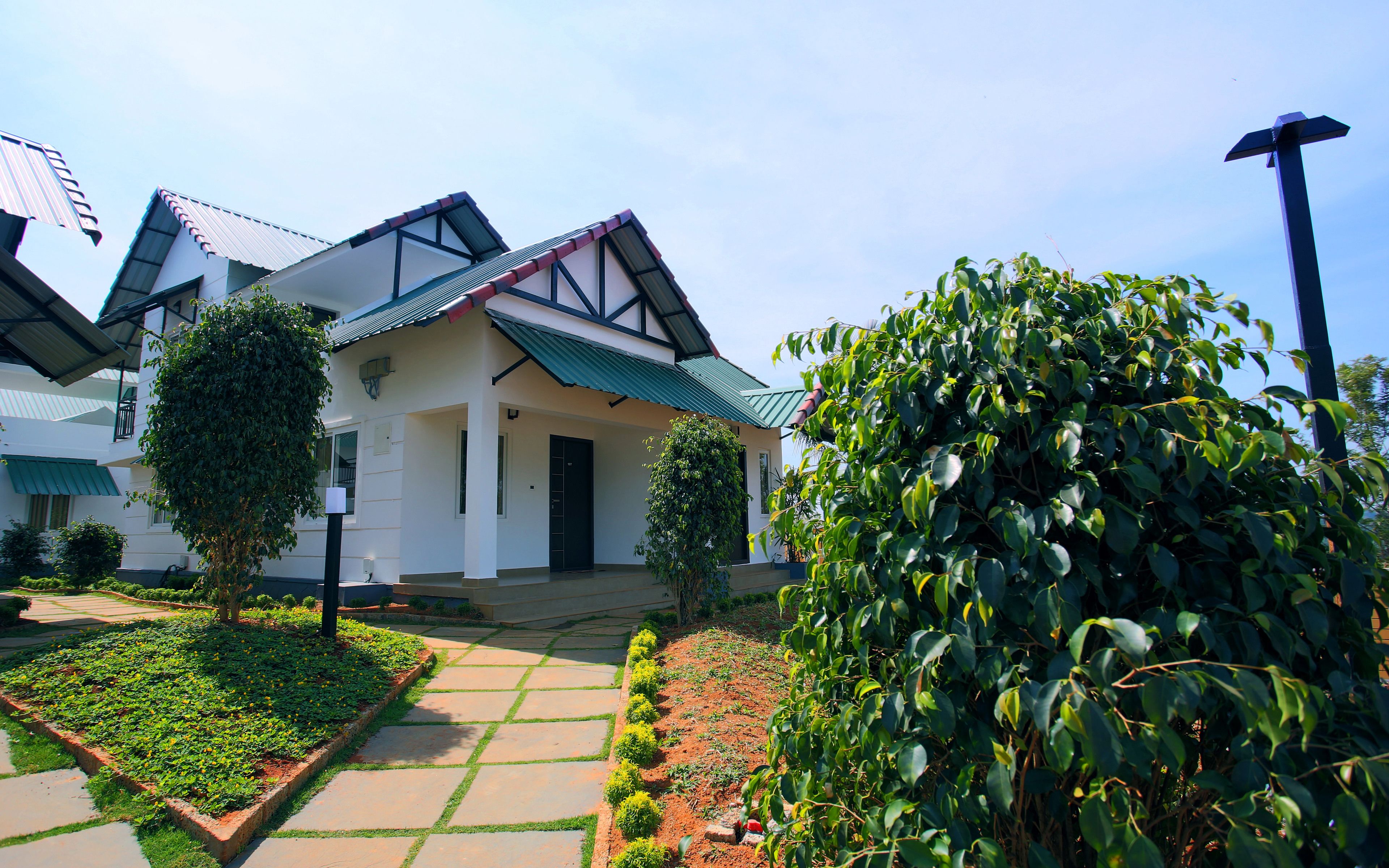A modern house with a green roof, a garden with a pathway, and a well-maintained lawn.