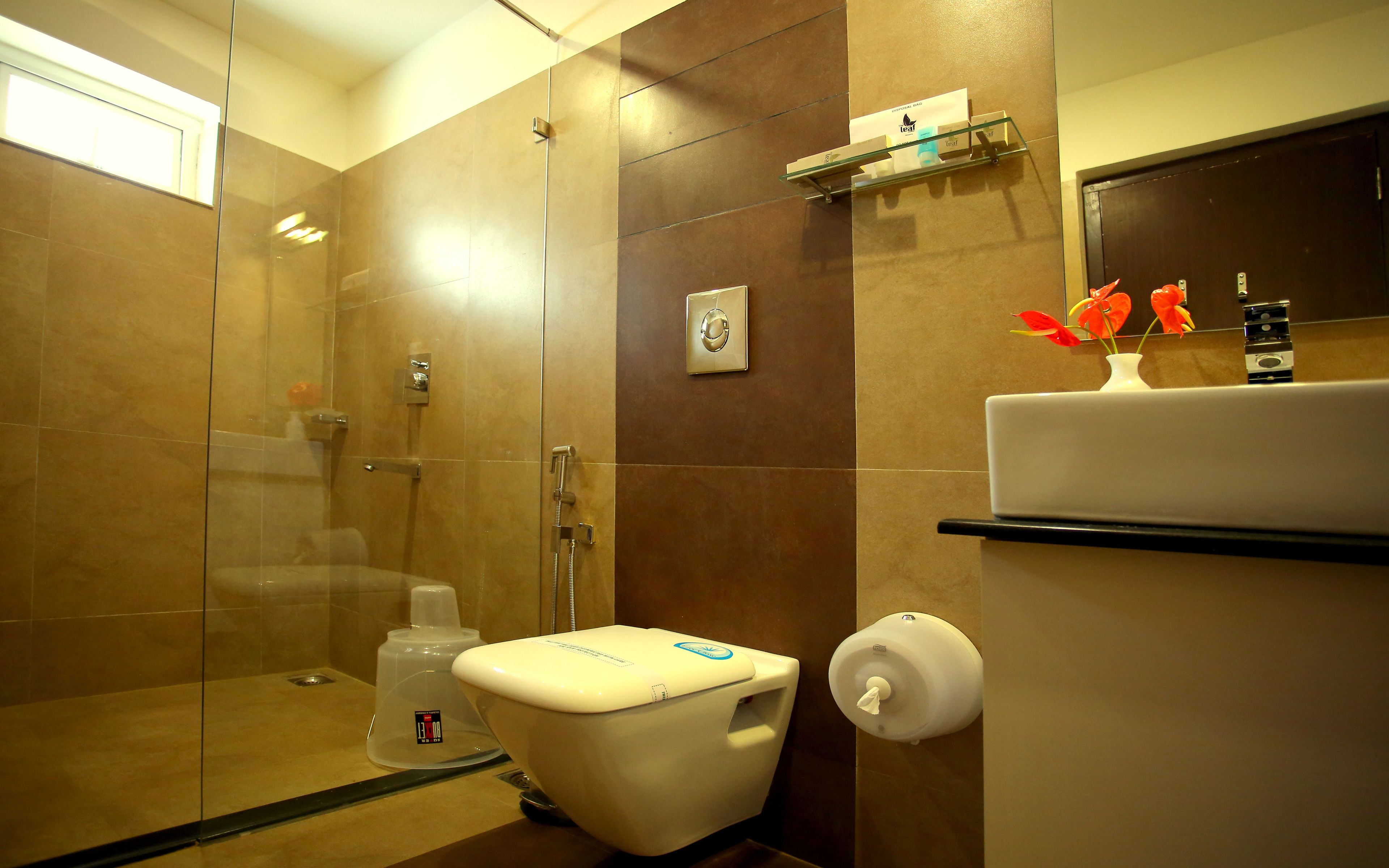 Een moderne badkamer met een douchecabine van glas, een toilet en een wastafel met zeepdispenser.