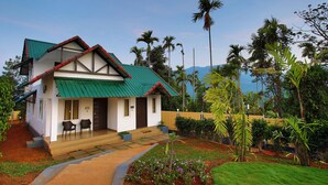 A two-story house with a green roof and a balcony, surrounded by lush greenery and palm trees. - The Leaf Munnar Resort (Devikolam)