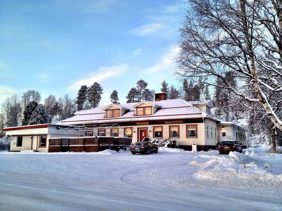 A two-story building with a snow-covered roof, a garage, and a parking area with two cars.