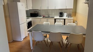 Cocina compacta con armarios blancos, horno empotrado, microondas, lavamanos y comedor con cuatro sillas.