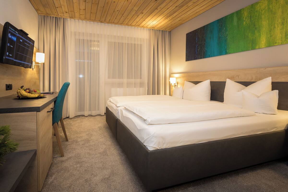 Hotellihuone, jossa on suuri sänky, työpöytä tuolilla, seinälle asennettu televisio ja sängyn yläpuolella oleva taulu.