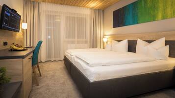 A hotel room with a large bed, a desk with a chair, a TV mounted on the wall, and a painting above the bed.