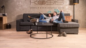 A modern living room with a grey sofa, a round coffee table, and a large flat-screen TV. - KOSIS Sports Lifestyle Hotel (Fuegen)