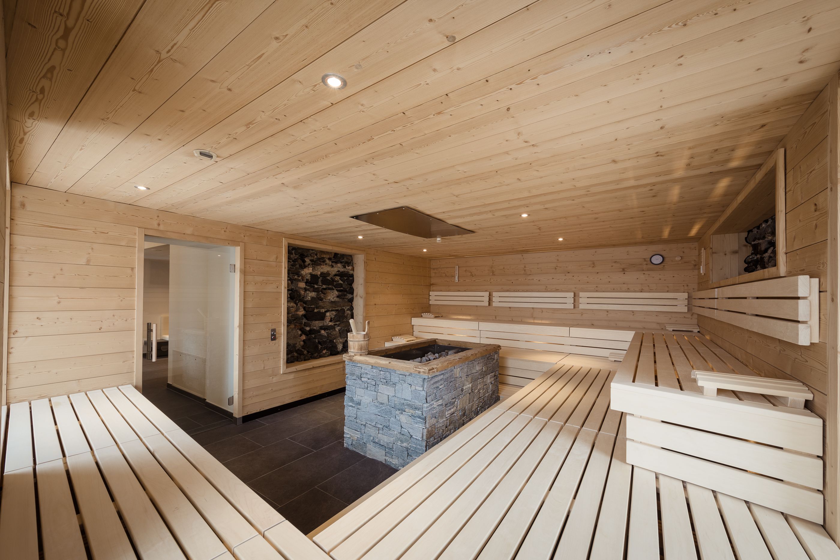 Eine Holzsauna mit Bänken und einem Kamin aus Stein.