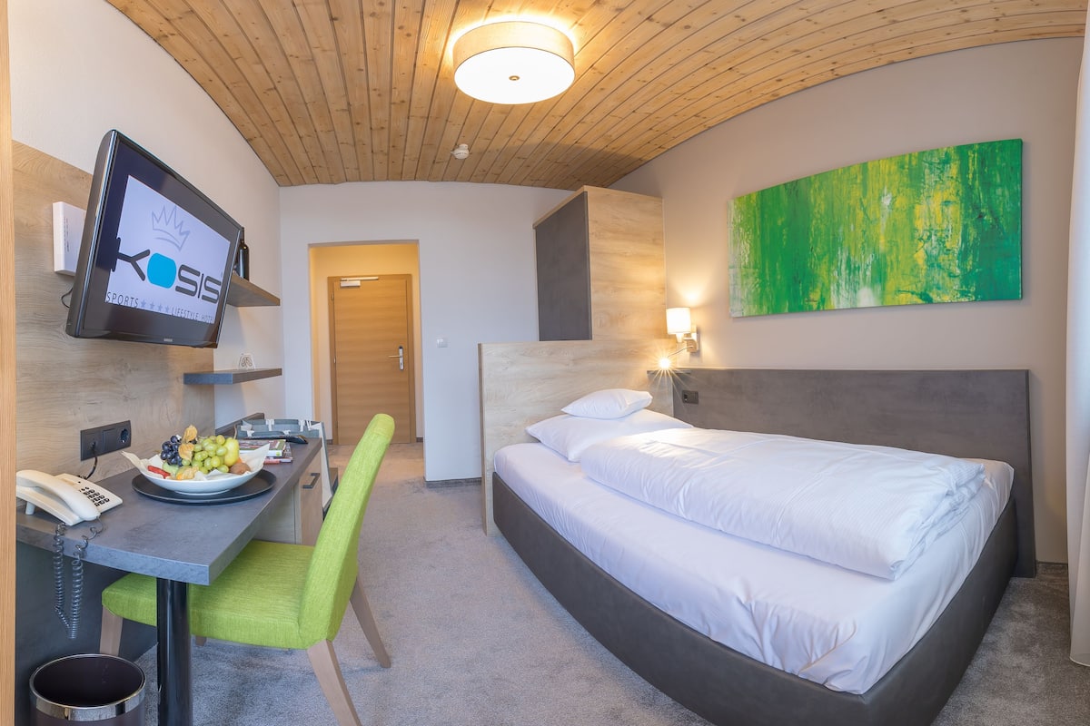 Hotellihuone, jossa on sänky, työpöytä tietokonenäytöllä, tuoli, puhelin ja seinälle asennettu televisio.