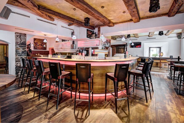 Un espace bar avec des tabourets de bar en bois, un comptoir central et un mur en pierre.