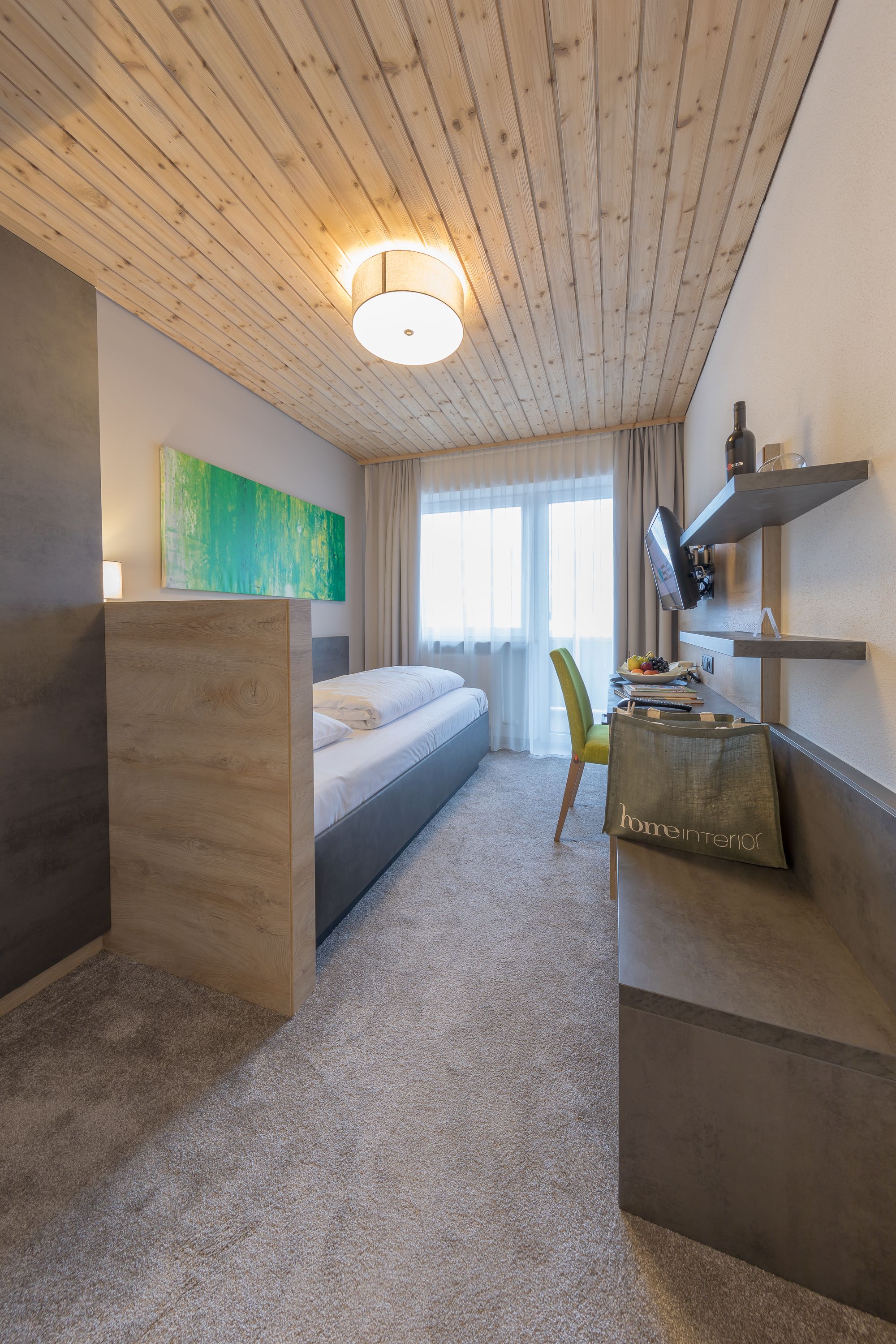 Habitación de hotel con cama, escritorio con silla, televisor y un cuadro abstracto verde en la pared.