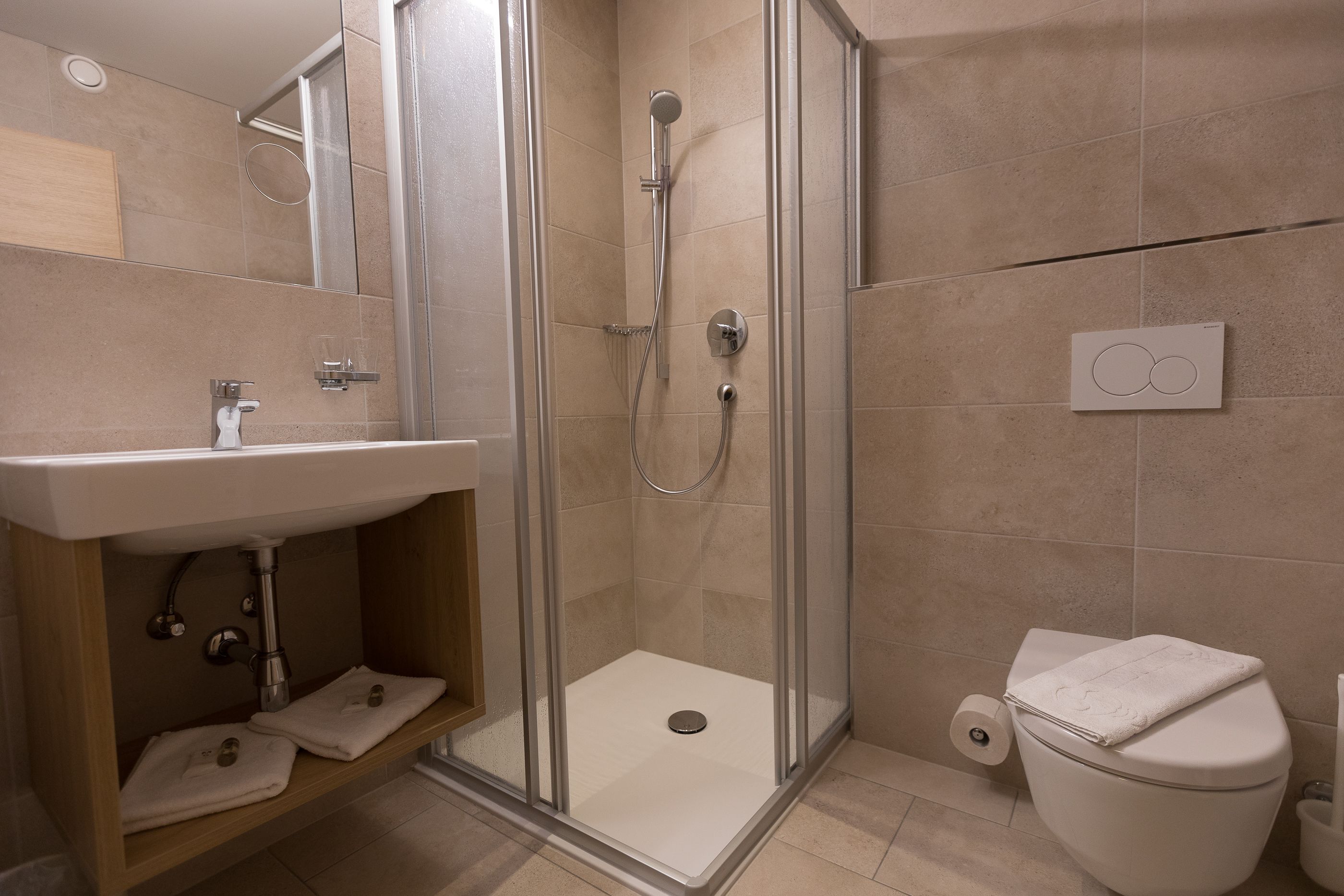 Un bany modern amb dutxa de vidre, un lavabo amb mirall i un vàter.