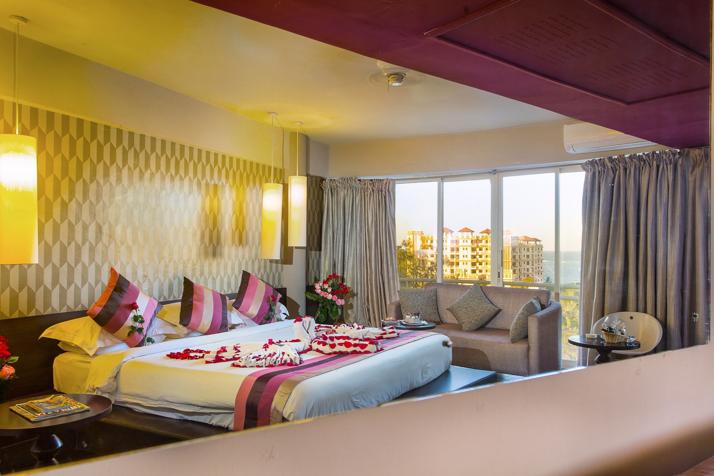 Una habitación de hotel con una cama grande, un sofá, una mesita y una ventana con cortinas.