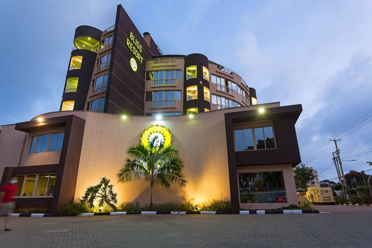 Um hotel moderno com um relógio em destaque na fachada, várias varandas e uma entrada bem iluminada.