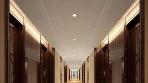 Un long couloir étroit, typique d’un hôtel, avec des portes en bois de chaque côté et un sol recouvert de moquette ornée de motifs floraux.