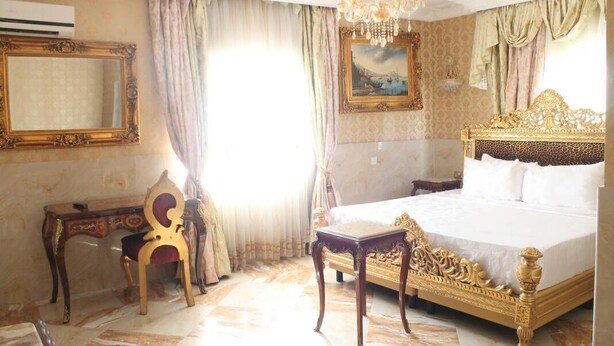 A hotel room with a large bed, a desk, a chair, and a chandelier. - Grand Emperor Hotel (Lekki)