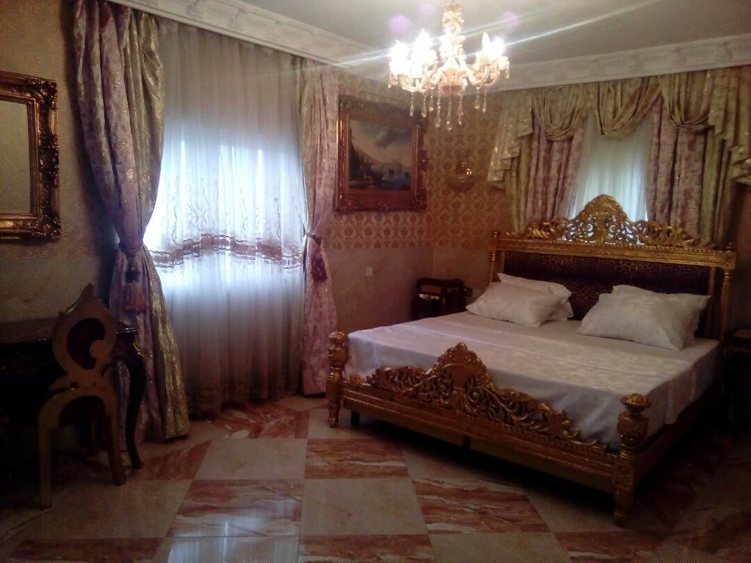 Un dormitorio con una cama grande y ornamentada, una araña y papel tapiz estampado.