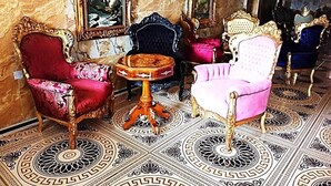 A luxurious room with ornate furniture, including a red and a pink chair, a round table, and a large painting on the wall. - Grand Emperor Hotel (Lekki)