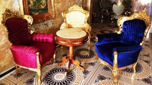 A room with ornate furniture, including two chairs with gold and blue upholstery, a round table, and a painting on the wall. - Grand Emperor Hotel (Lekki)