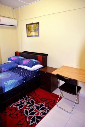 A bedroom with a bed, a desk, a chair, a red and black patterned rug, and a wall-mounted air conditioner. - Awedee Homestay Putrajaya (Putrajaya)
