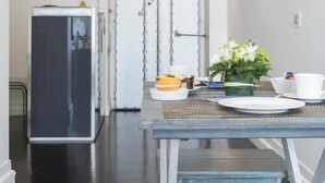 Un comedor con una araña, una mesa con platos y un florero, y un refrigerador al fondo.