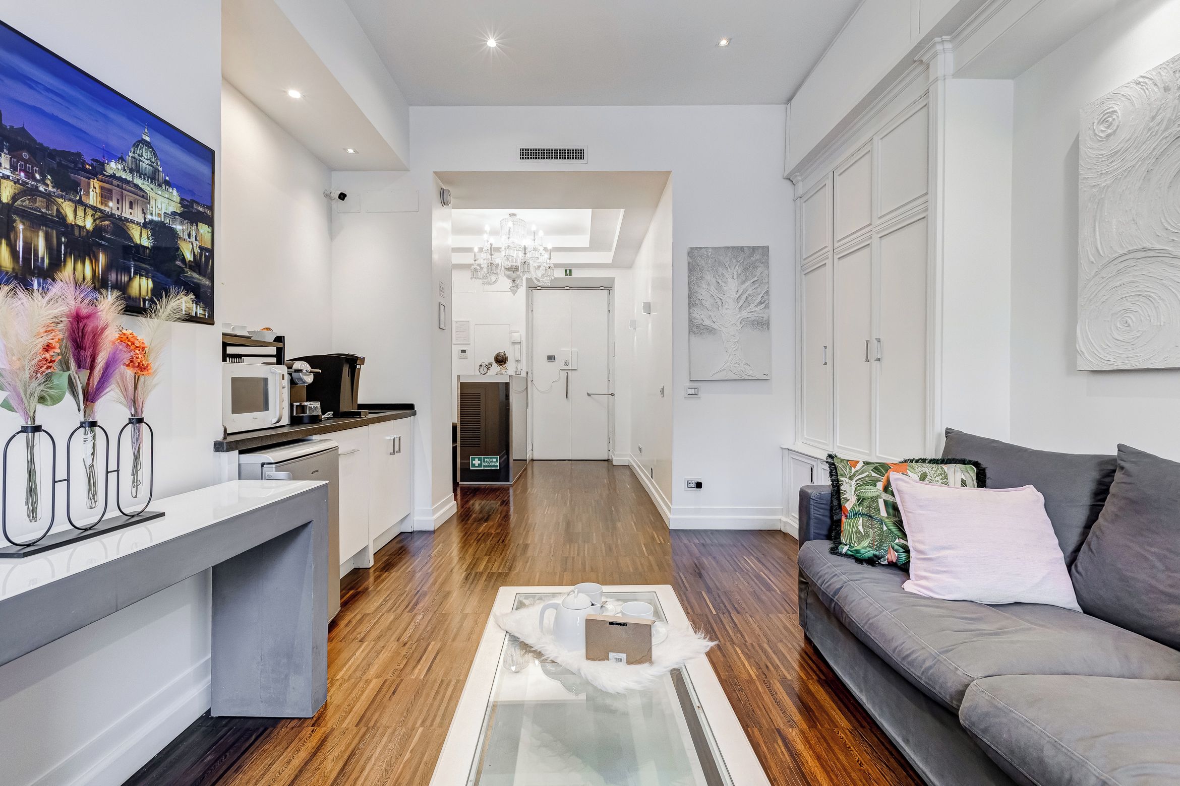 A modern living room with a grey sofa, a coffee table, and a kitchen area with a microwave.