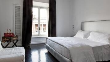 Una habitación de hotel con una cama grande, una mesita con un bolso rojo y una ventana con cortinas.