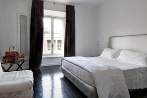 A hotel room with a large bed, a small table with a red bag, and a window with curtains. - Xenia Guest House (Rome)