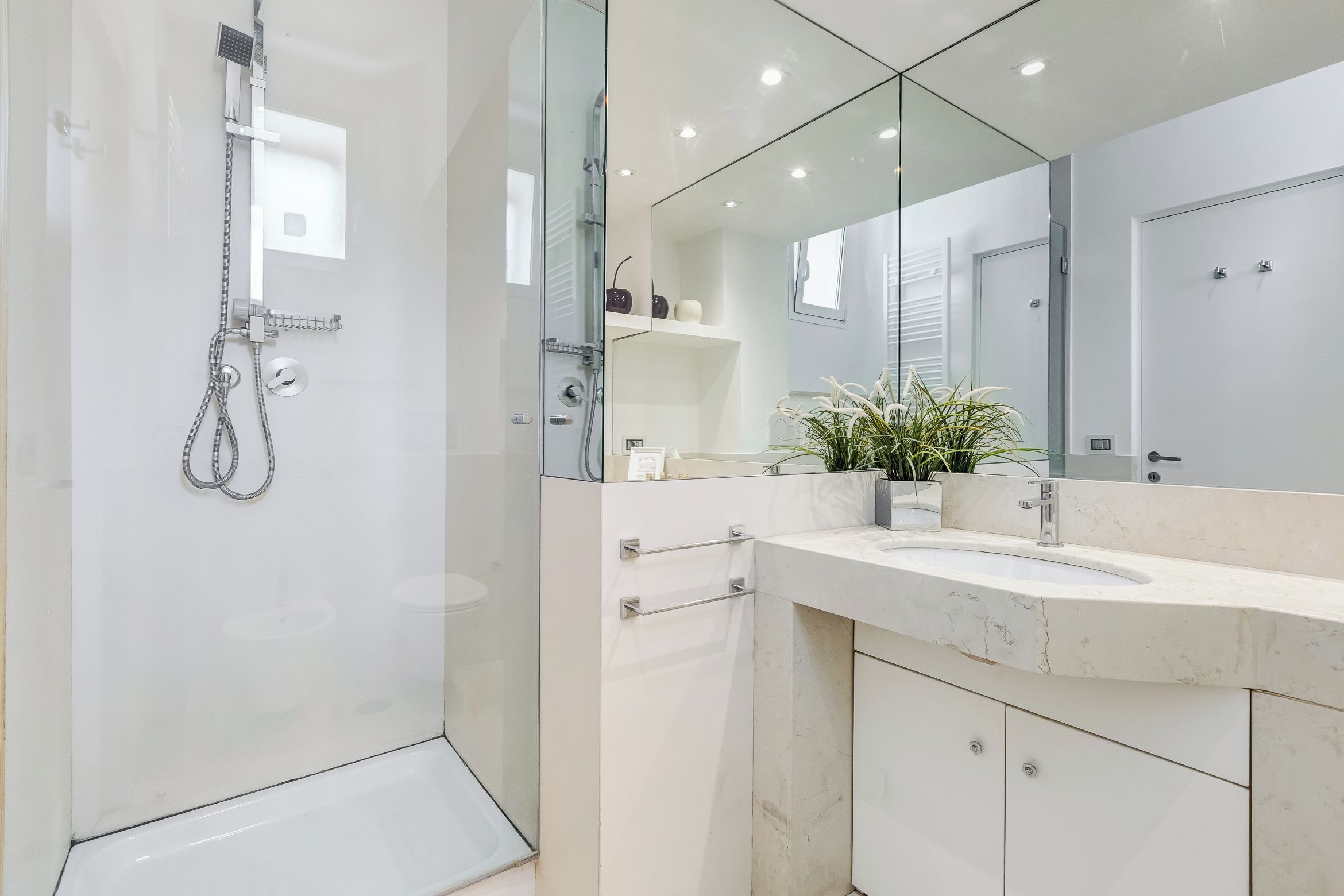 Un baño moderno con cabina de ducha de vidrio, un espejo grande y un tocador de mármol.