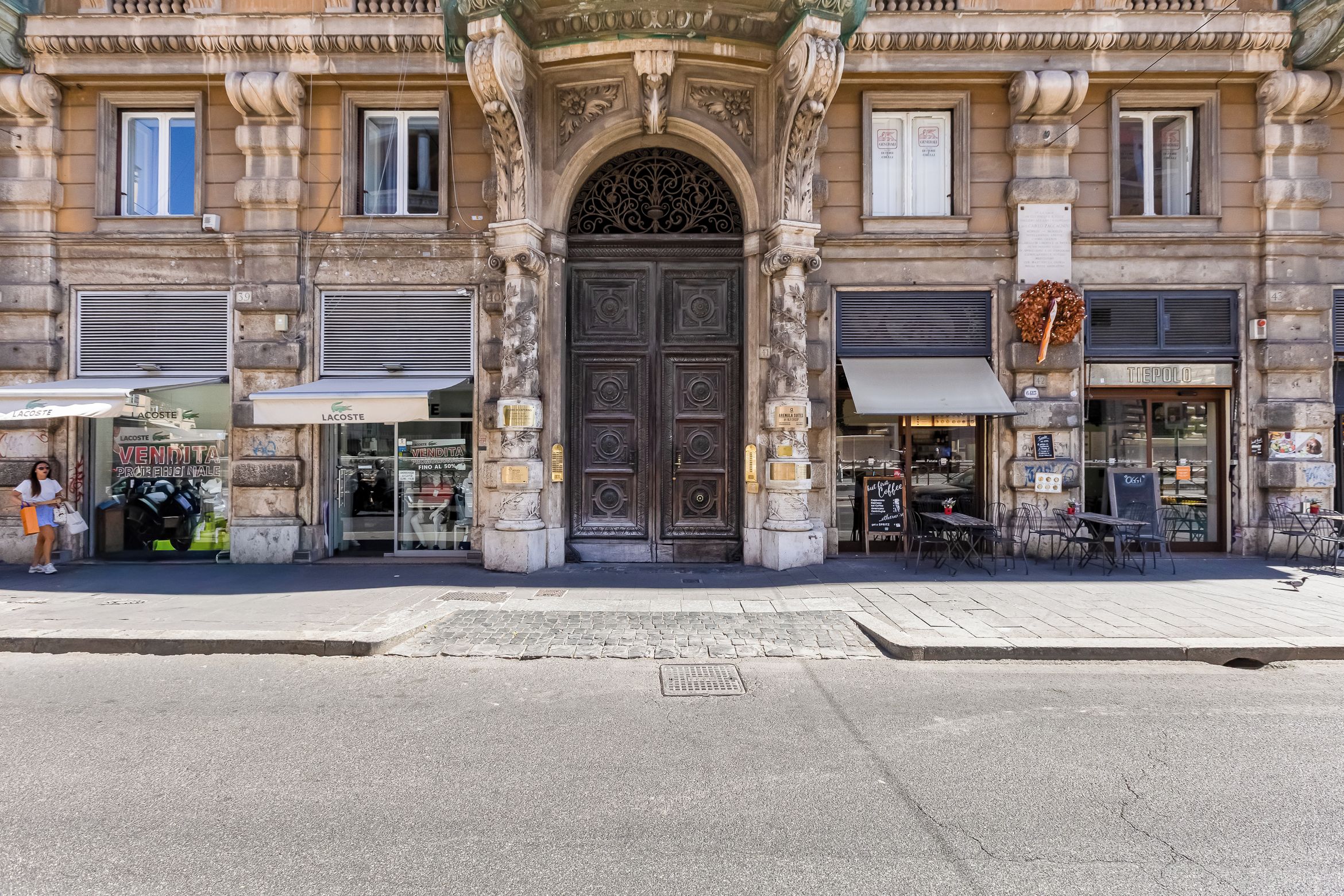 Un edificio histórico con una entrada central ornamentada, tiendas a ambos lados y mesas al aire libre.