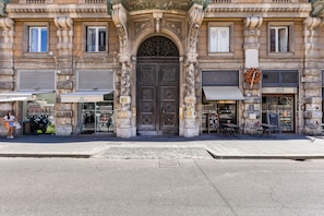 Un edificio histórico con una entrada central ornamentada, tiendas a ambos lados y mesas al aire libre.