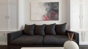 Una sala de estar moderna con un sofá gris oscuro, una mesa de centro de vidrio y un jarrón blanco con ramas.
